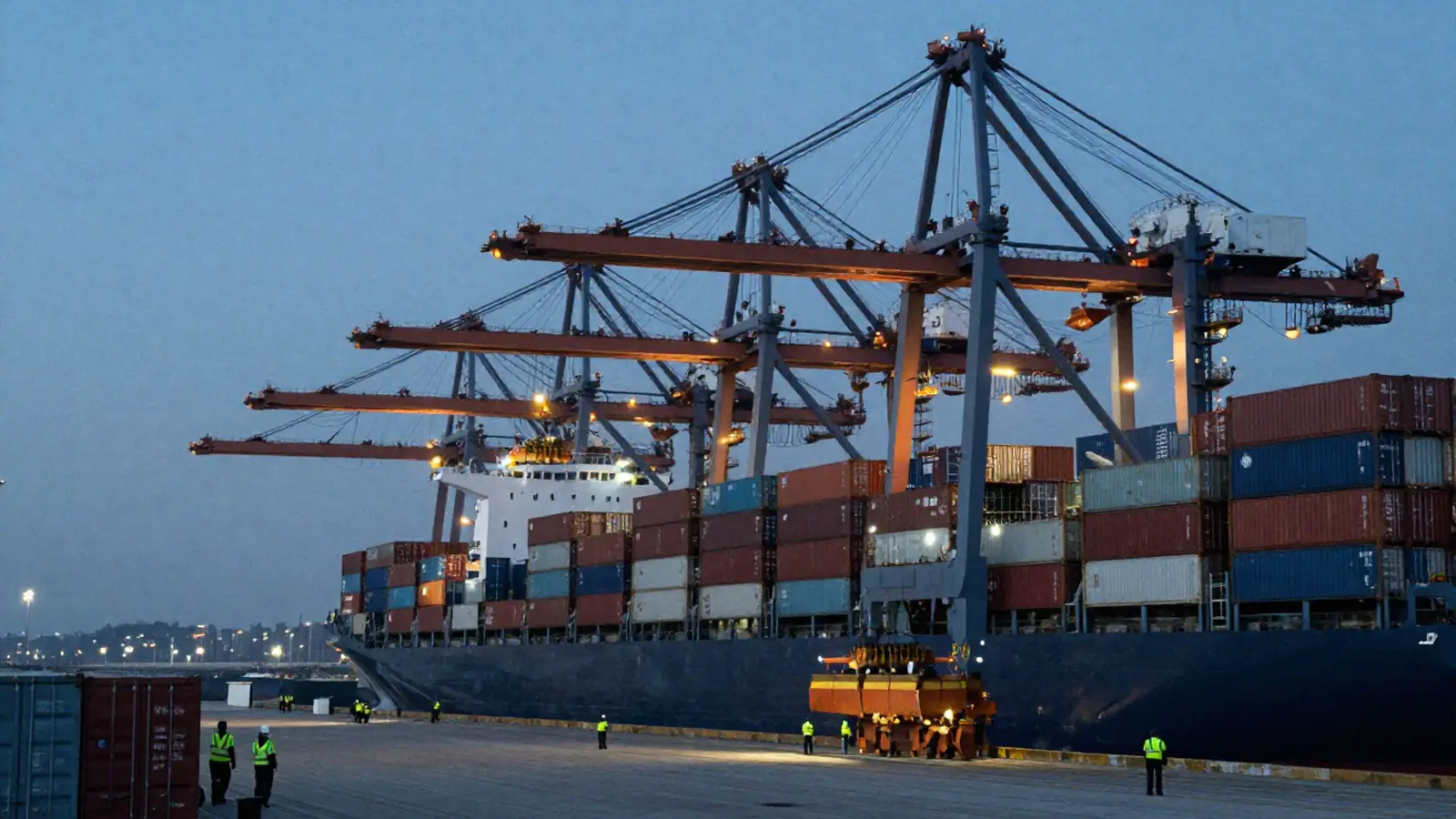 Puerto de contenedores al anochecer con grúas cargando un buque y trabajadores en primer plano